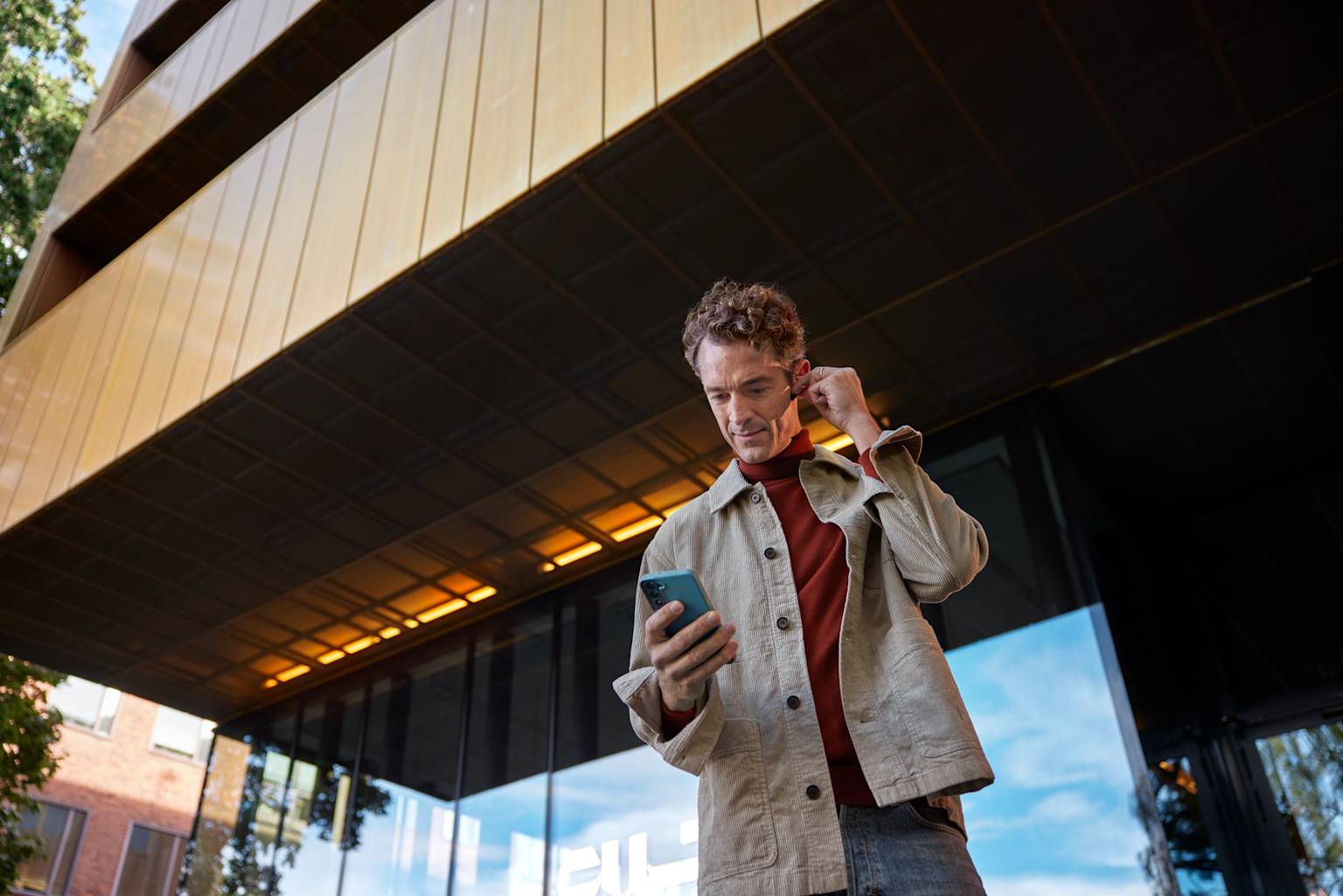 Man med hörlurar och mobil framför en byggnad