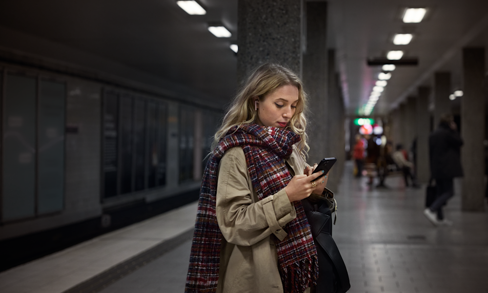 Kvinna på tunnelbaneperrong som tittar på sin mobiltelefon