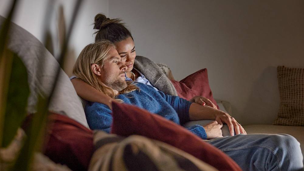 Ett yngre par sitter tillsammans i soffan och tittar på tv.