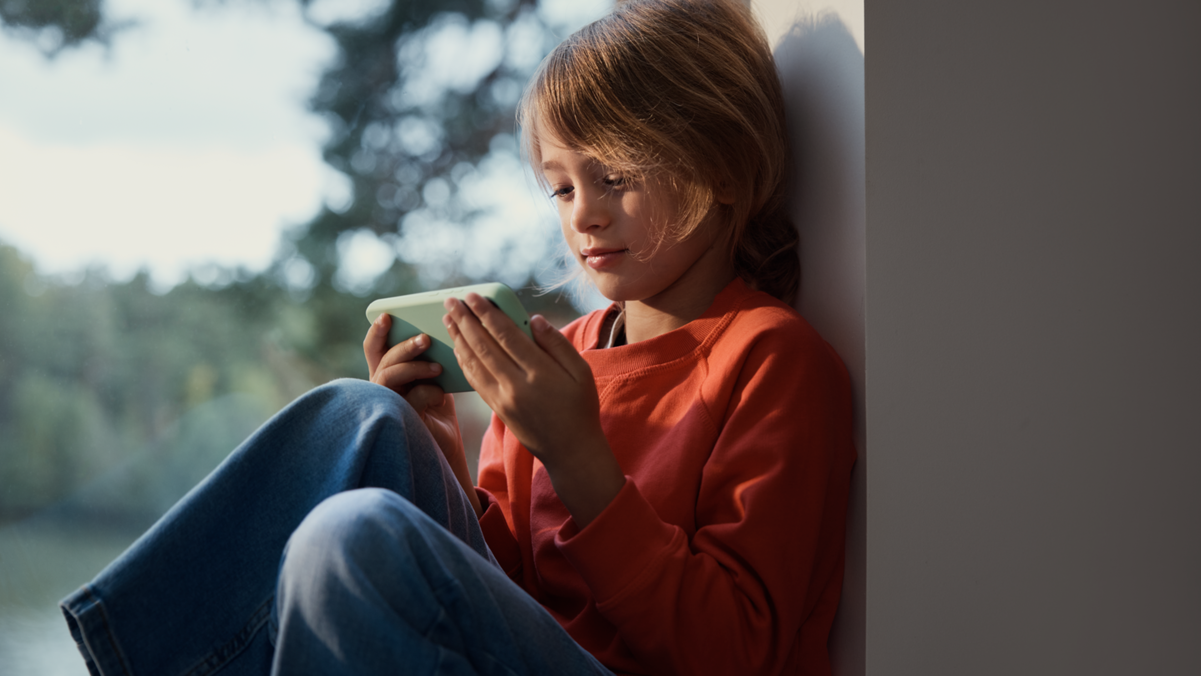 Barn sitter i fönstret och tittar på en mobiltelefon.