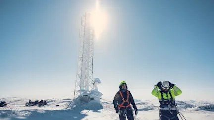 Här syns en mobilmast tillsammans med två medarbetare från Telia i blåställ någonstans i ett härligt vintrigt snölandskap med glänsande sol i fjällen.