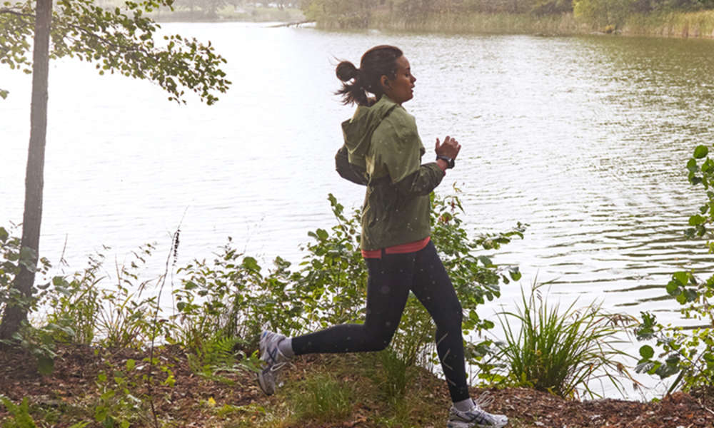 Kvinna joggar i skogen framför sjö.