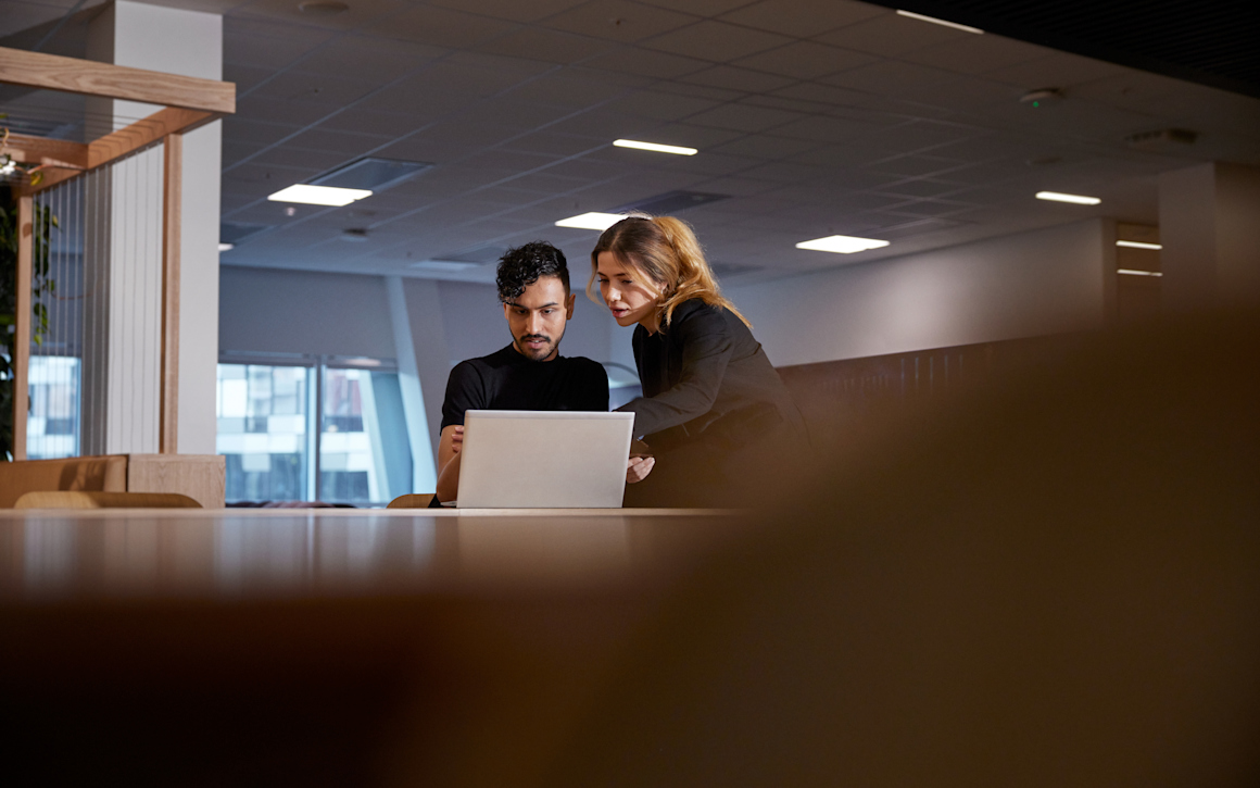 Kvinna pekar på datorskärm för att visa en man något på hans dator.