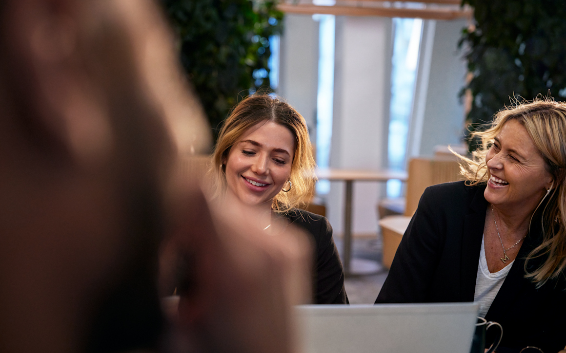 Kvinnor skrattar framför laptop på kontor.