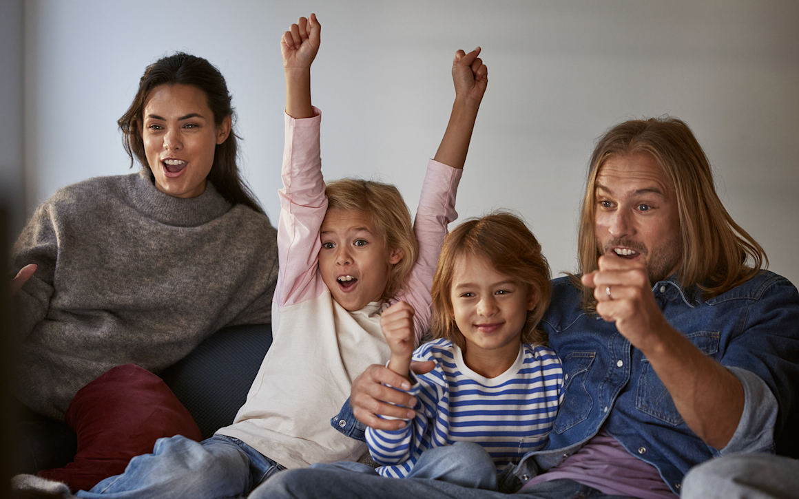 En glad familj tittar på tv och äter popcorn.
