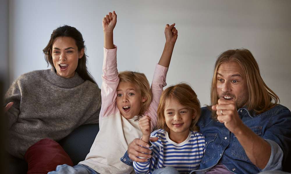 En glad familj tittar på tv och äter popcorn.