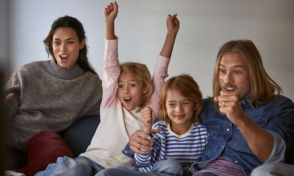 Familj med mamma, pappa och två barn sitter framför tv:n och hejar på sitt lag. Upptäck tv och streaming från Telia.