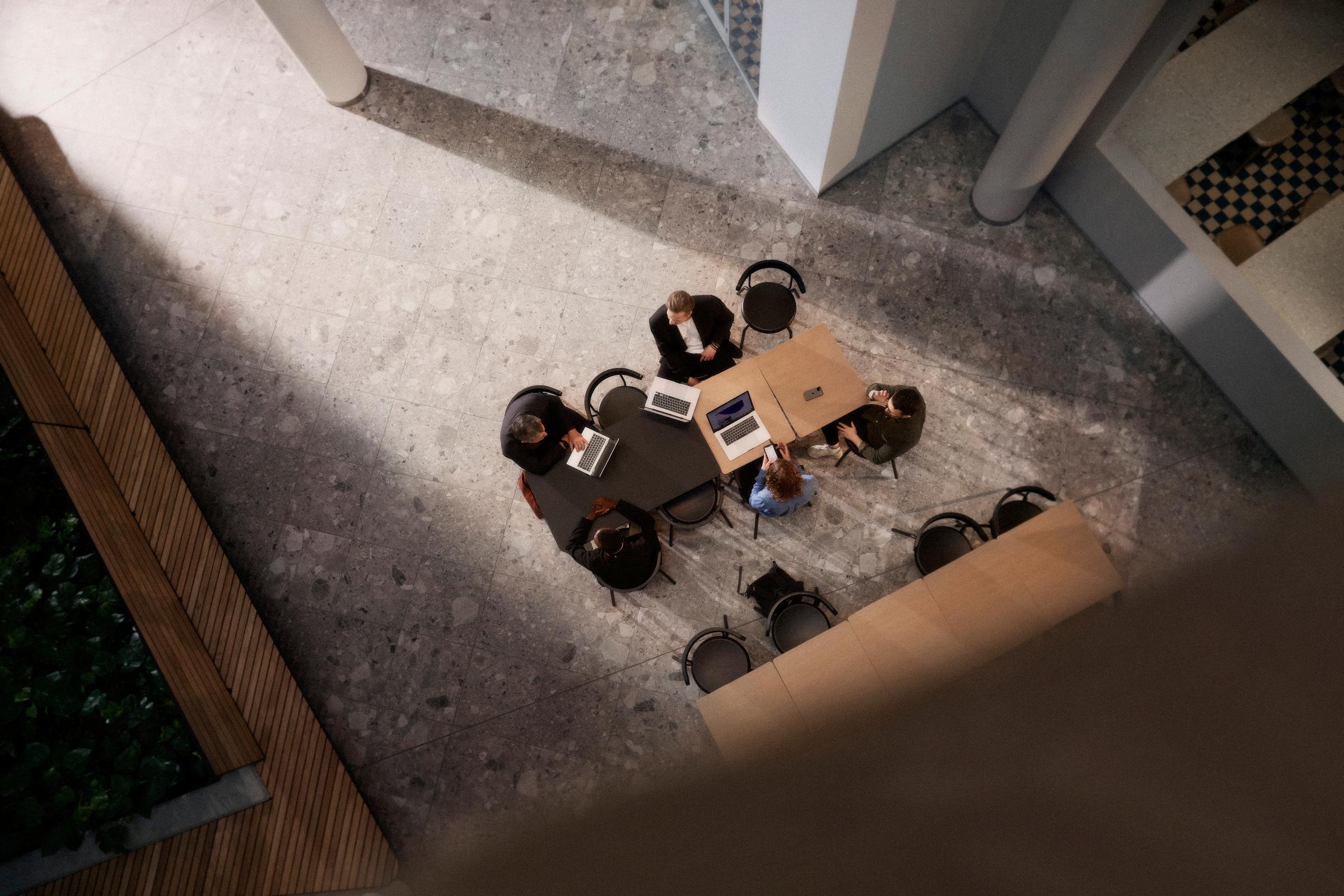 Konferensbord med arbetande människor och datorer sett ovanifrån.