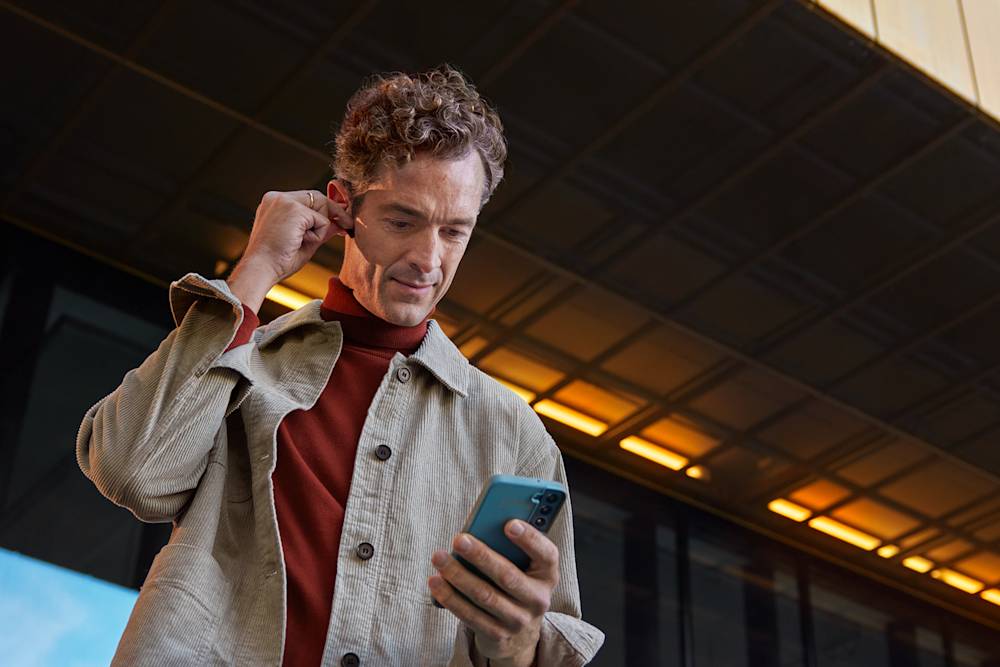 Man i beige skjorta tittar i mobilen