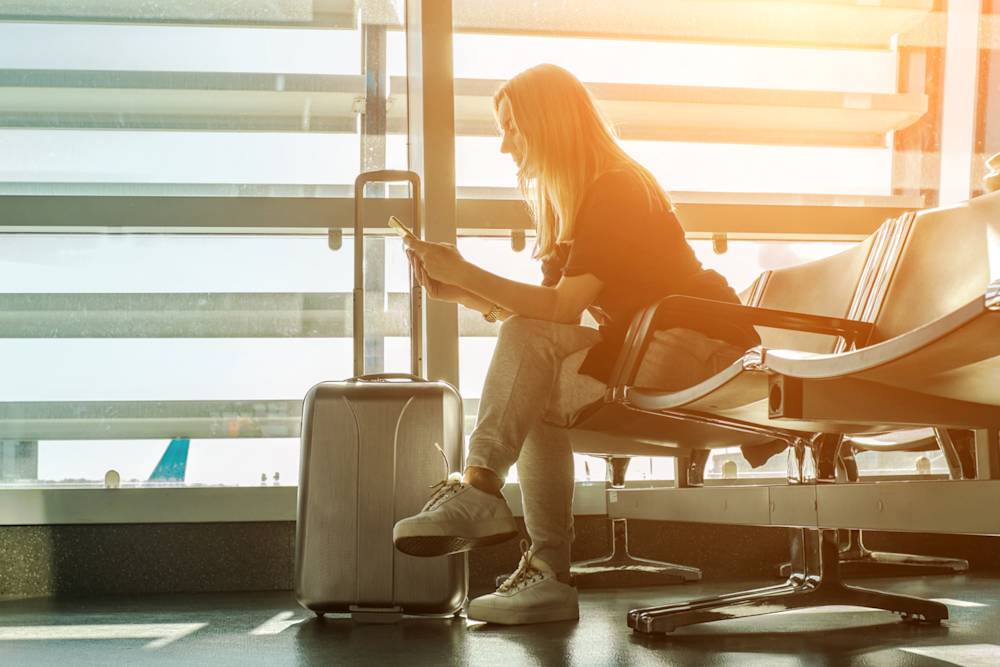 Kvinna sitter på flygplats och tittar i mobilen