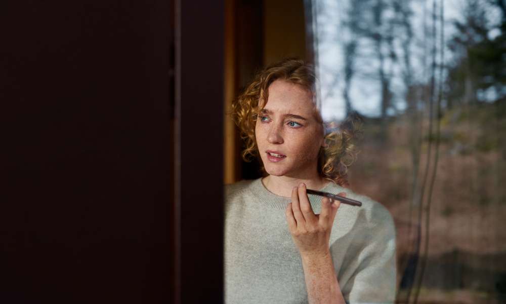 Kvinna talar i mobilen intill ett fönster