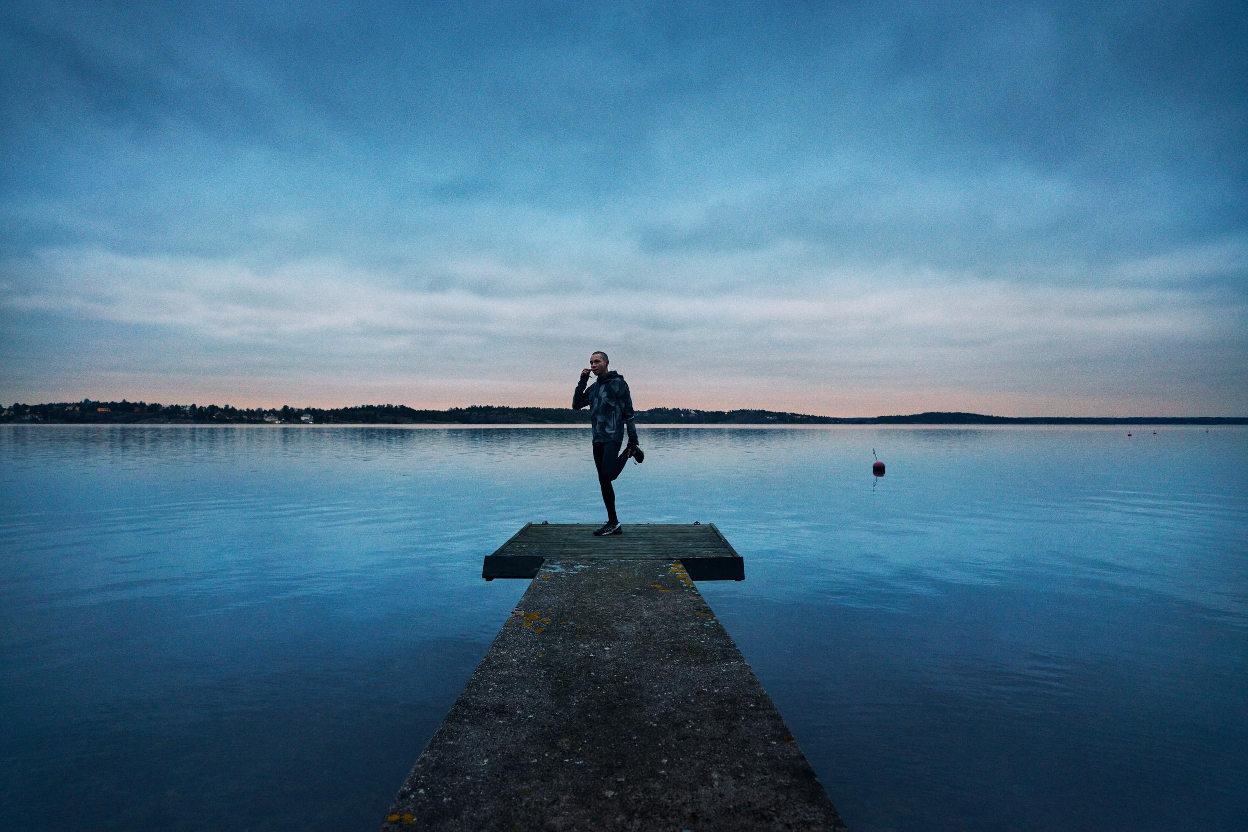 Man stretchar på brygga och pratar i mobiltelefon på kvällen.