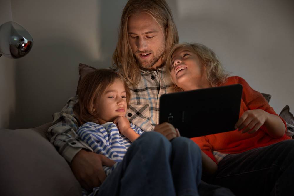 Bild på pappa med barn i soffa med surfplatta