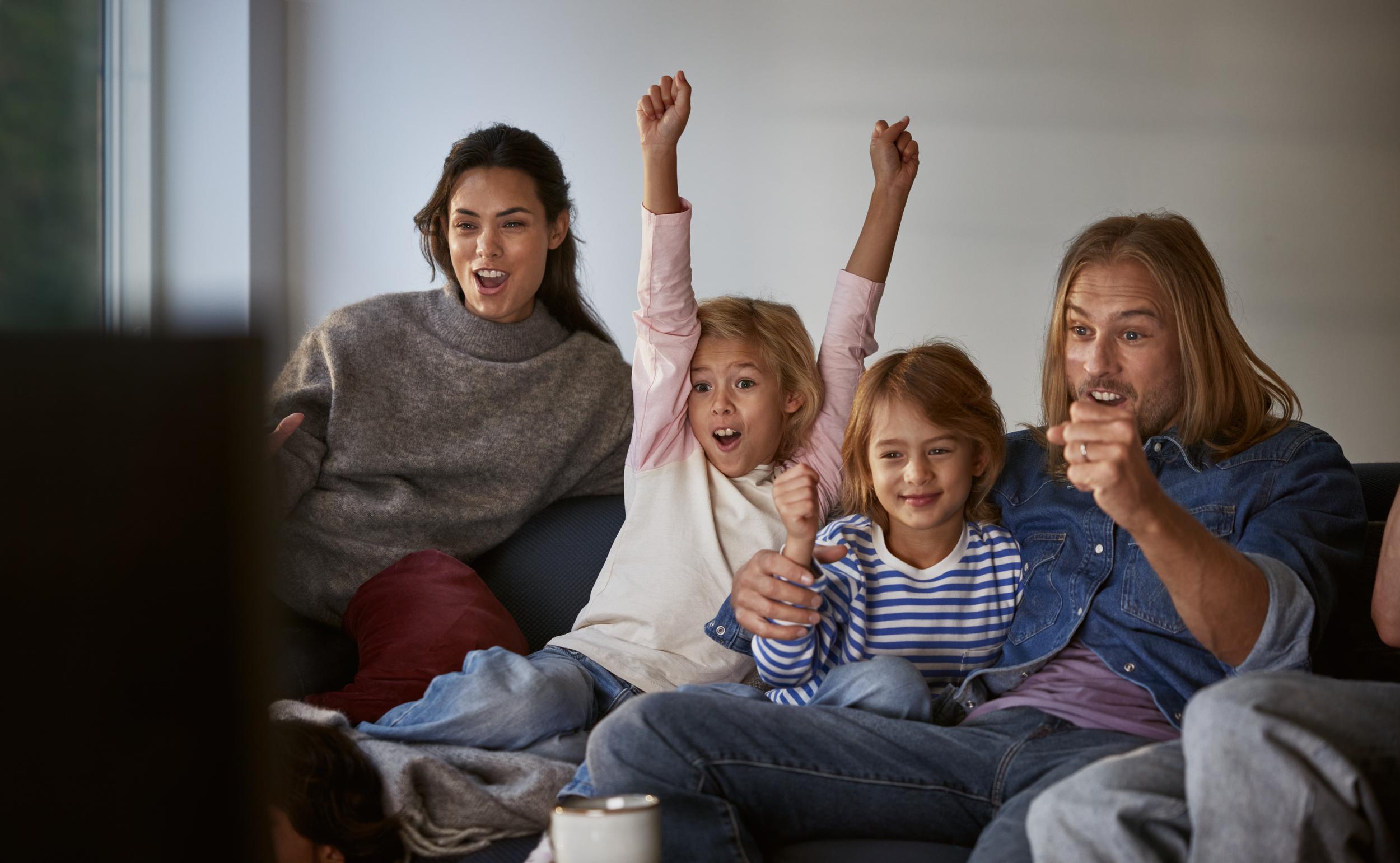 Familj med mamma, pappa och två barn sitter framför tv:n och hejar på sitt lag. Upptäck tv och streaming från Telia.