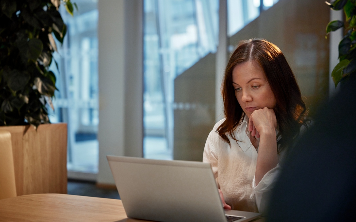 Kvinna arbetar vid dator framför ett fönster.