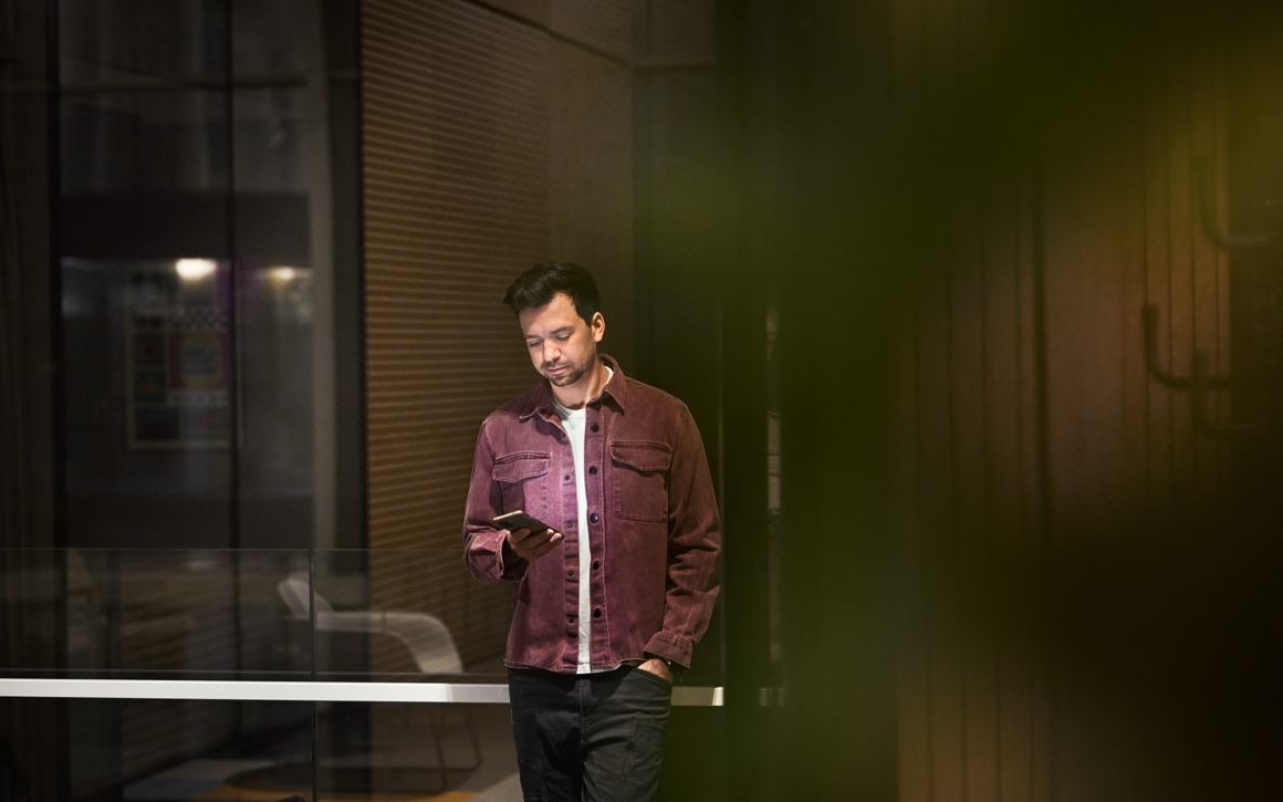 Avslappnat klädd man håller i telefon med företagsabonnemang på kontor