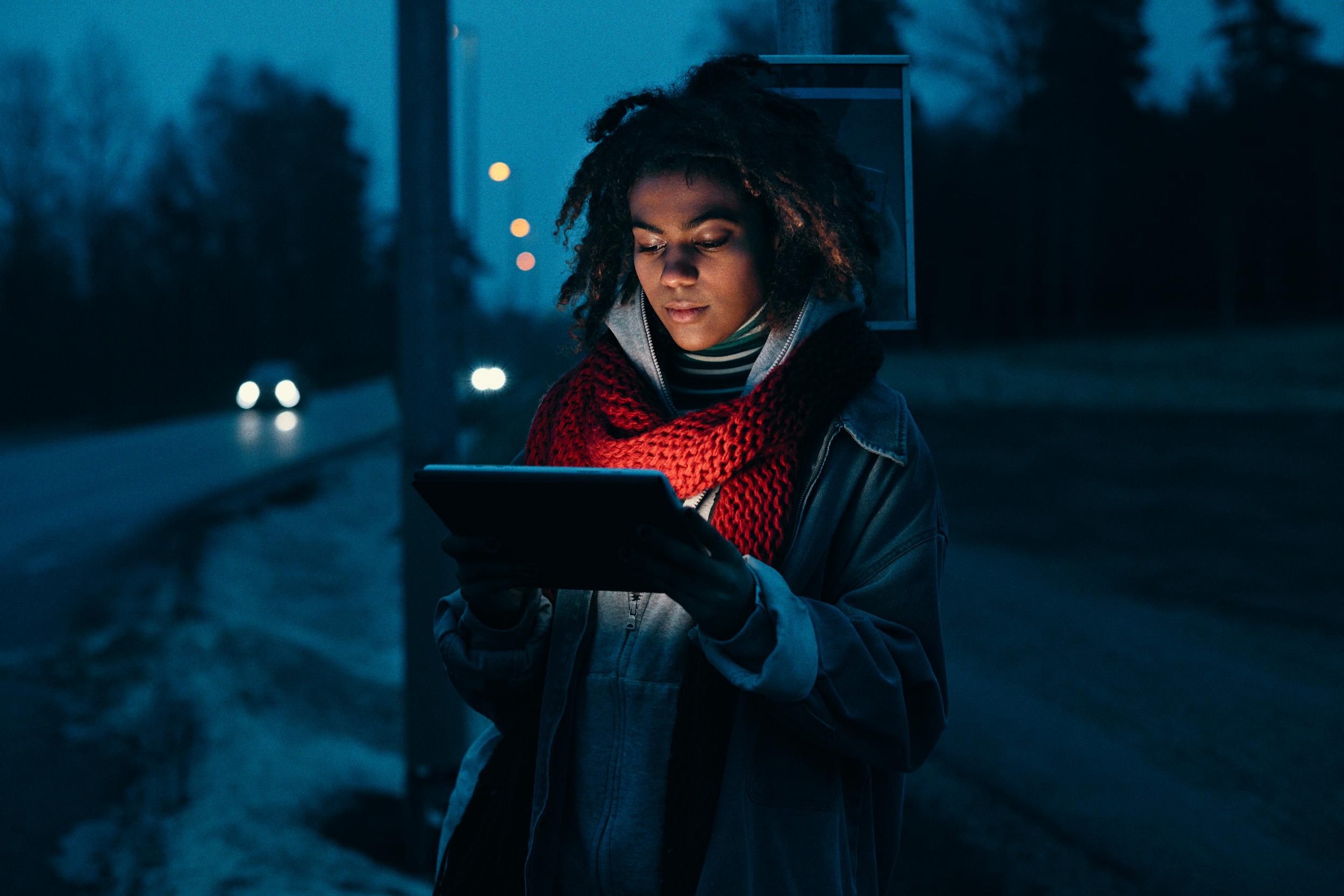 Tjej med surfplatta vid busshållplats.