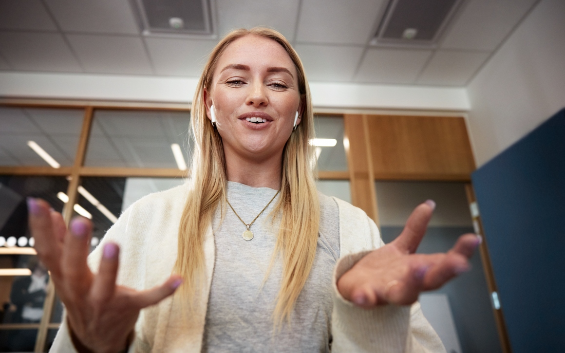 Ung kvinna med Airpods och beskrivande händer på kontor.