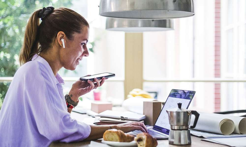 Kvinna med mobiltelefon arbetar vid laptop.