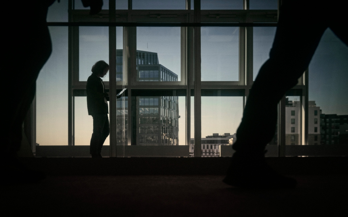 Silhuett av man som går framför kontorsfönster i ett mörkt rum