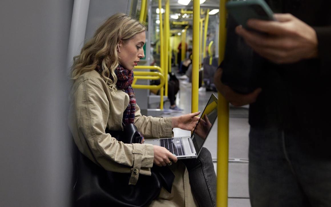 Kvinna sitter på tåg i Stockholms tunnelbana med en bärbar dator i knät.