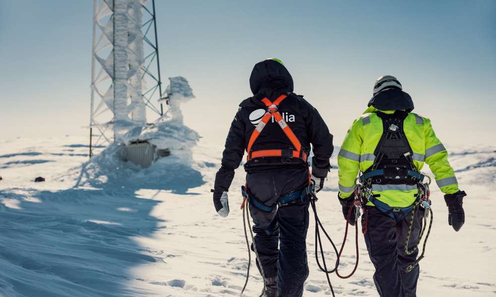 Arbetare i snöigt landskap framför mobilmast.