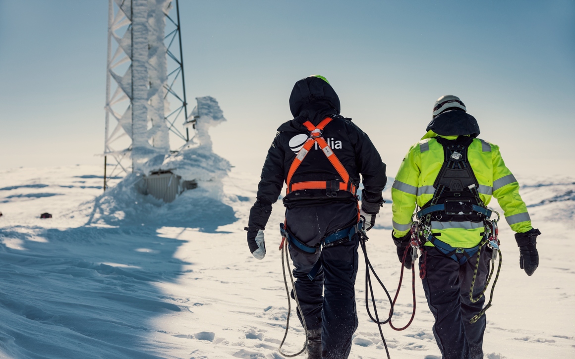Två män går i snö mot en mast