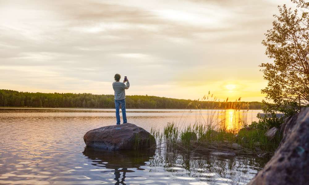 Kvinna som står på en liten holme och fotograferar solnedgången