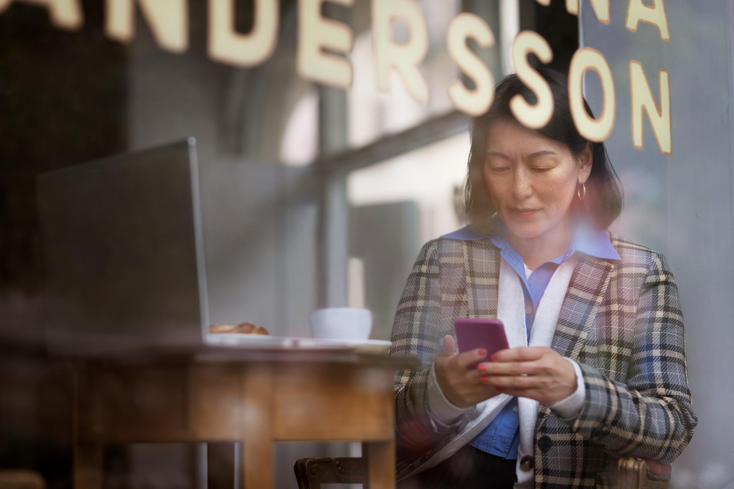 Kvinna bakom skyltfönster som står och kollar ner i sin mobiltelefon
