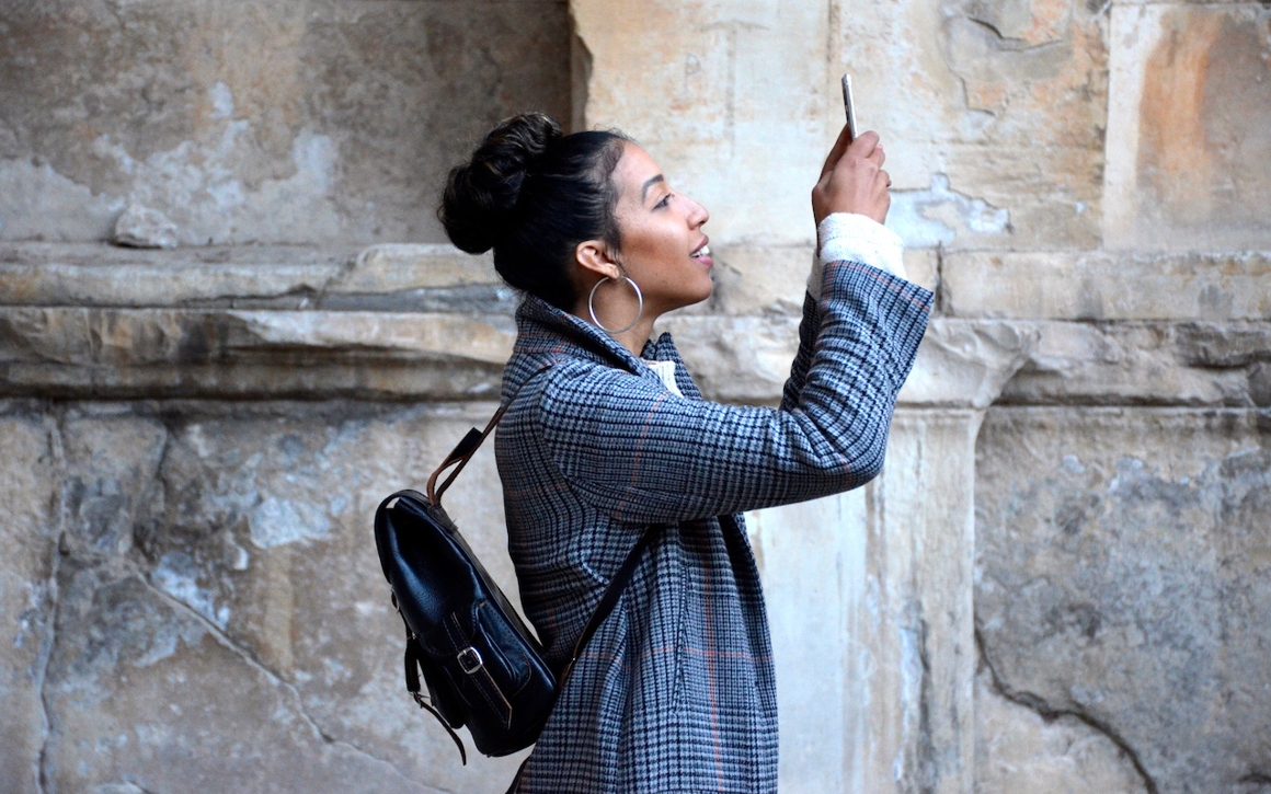 En kvinna med ryggsäck tar en bild med sin mobil.